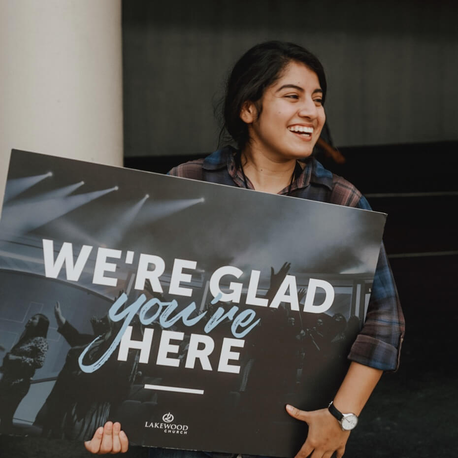 Greeter holds "we're glad you're here" sign