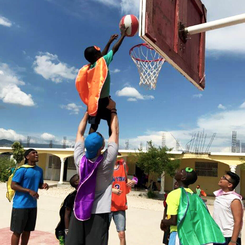 A volunteer helps a child reach a basketball hoop during a mission trip to Haiti.