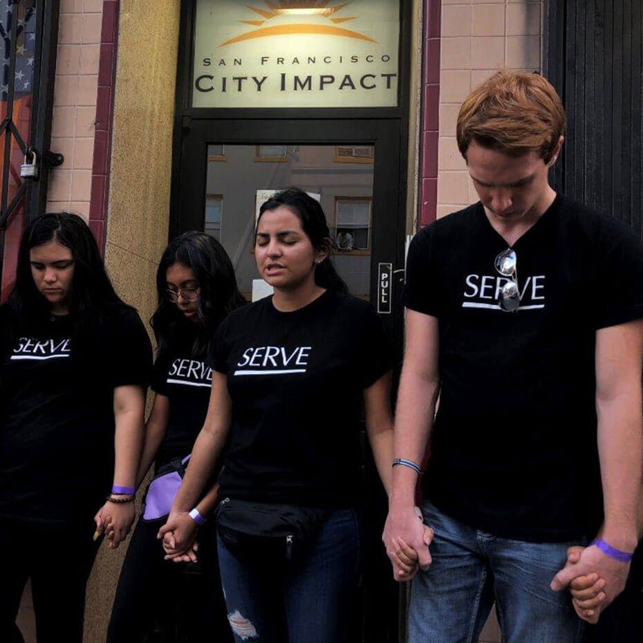A group of teens prays in front of a building during a mission trip to San Francisco.